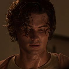 a young man with wet hair stares into the distance while standing in a dimly lit room