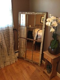 a mirror sitting on top of a wooden floor next to a vase filled with flowers