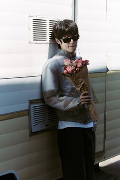 a young man is holding flowers in front of an rv door with the sun shining on him