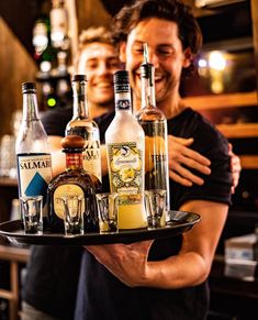 two men holding a tray with liquor bottles on it