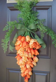 an orange flower hanging on the front door with greenery around it's edges