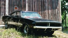 an old muscle car parked in front of a barn