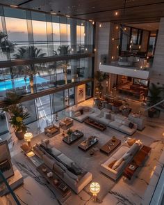 a large living room with couches and tables in front of the ocean at sunset