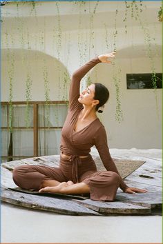 a woman sitting on top of a wooden floor in a yoga pose with her arms stretched out