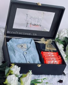 an open box with some items in it on a white blanket and flowers behind it