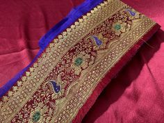 a red and blue sari laying on top of a pink cloth covered in gold thread