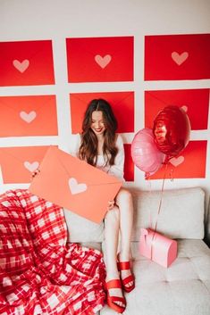 a woman sitting on top of a couch holding up two red and pink hearts balloons