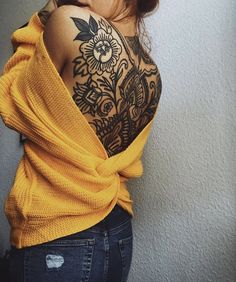 a woman with a flower tattoo on her chest and shoulder wrapped in a yellow sweater