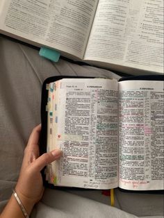 an open bible on top of a bed next to a woman's hand holding it