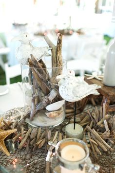 a glass vase filled with driftwood on top of a table next to a candle