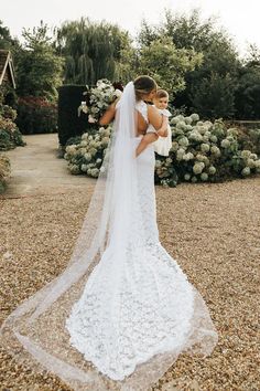 a woman in a wedding dress holding a baby and looking at the bride's veil