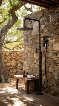 an outdoor shower is shown in front of a stone wall and bench under a tree