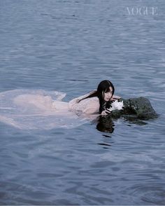 a woman floating on top of a body of water next to a rock in the ocean