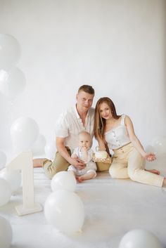 a man, woman and baby sitting on the floor with balloons around them in front of white backdrop