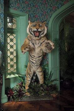 a large stuffed tiger standing in front of a green door with its mouth wide open