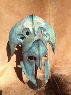 a blue mask with an open mouth on a brown surface and a shadow from the wall behind it