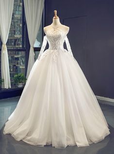 a white wedding dress on display in front of a window with curtains and drapes