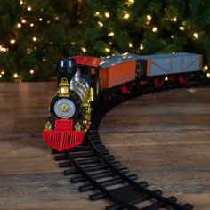 a toy train is coming down the track in front of a christmas tree with lights