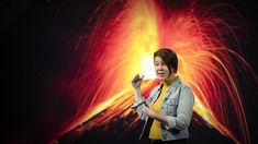 a woman standing in front of a large screen with fireworks on the wall behind her