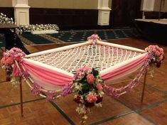 a white hammock with pink and purple flowers on the front is set up for a wedding ceremony