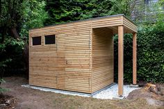 a small wooden shed sitting in the middle of a yard next to some bushes and trees