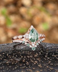 an engagement ring with green and white stones on top of a piece of rock in the woods