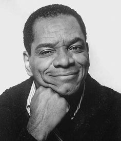 a black and white photo of a smiling man with his chin resting on his hand