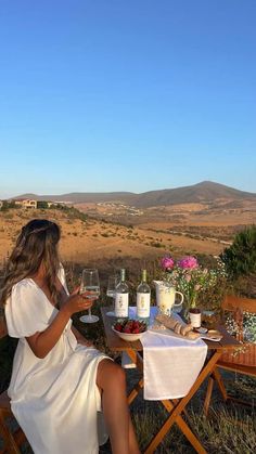 a woman sitting at a table with wine glasses in front of her and looking out into the distance