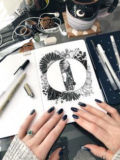 a woman's hands on top of a notebook surrounded by various pens and pencils