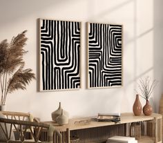 two black and white paintings hanging on the wall above a wooden table in a living room