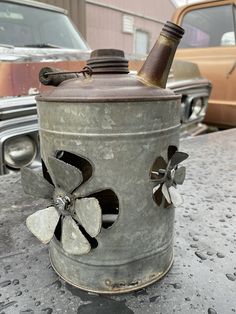 an old metal can with flowers on it sitting on a table next to a car