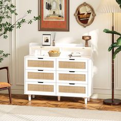 a white dresser sitting in a living room next to a potted plant and lamp