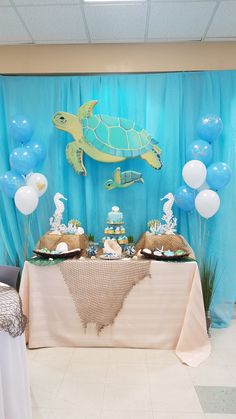 a table topped with cake and balloons next to a blue wall covered in sea animals