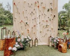 an outdoor wedding setup with flowers on the wall and wooden stumps in front of it