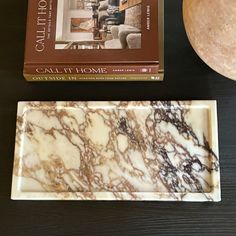 a marble plate sitting on top of a wooden table next to a book and bowl