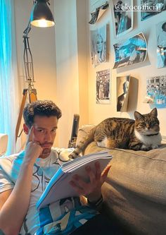 a man sitting on a couch reading a book with a cat laying next to him