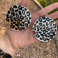 a hand holding two animal print brooches on top of each other in front of a gravel area