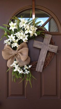 a wreath with white flowers and a cross hanging on the front door to welcome people