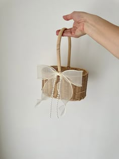 a hand is holding a basket with white ribbon and bows on the handle, hanging from a wall