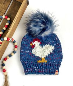 "This is a super cute Chicken Beanie, hand knit out of Lion Brand Wool Ease Super Bulky yarn in Firecracker with a 6\" Stonewashed faux fur pom pom that is detachable. This is an adult women's size and measures approximately 9\" in length, not including the pom. The hat can be washed, I recommend hand wash. lay flat to dry. The pom is not washable and is attached with a snap that makes it super secure but also very easy to remove.  The yarn is 20% wool 80% acrylic **Wood box and beads are photo Whimsical Hand Knitted Hats, One Size, Whimsical Hand-knitted Hats, Handmade Cozy Hat One Size Fits Most, Country Style Winter Cap, Winter Country Style Hat One Size, Handmade Blue Fall Hats, Fun Knitted Hat, One Size Fits Most, Cute Knitted One Size Hats, Fun Hand Knitted One Size Hats