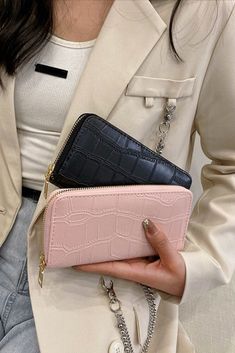 a woman holding a pink and black purse in her right hand while wearing a beige blazer