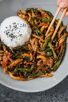 someone is holding chopsticks over a bowl of stir fry with rice and vegetables