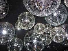 many shiny disco balls hanging from the ceiling in front of a black wall with lights