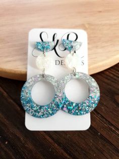 two pairs of blue and white earrings on top of a wooden table next to a card