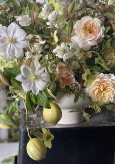 a vase filled with flowers and fruit on top of a table