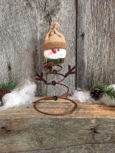 a small snowman with a hat on top of a wooden table next to pine cones