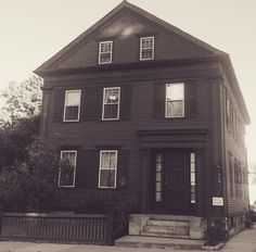 a black and white photo of a house with two windows on the second floor, stairs leading up to the front door