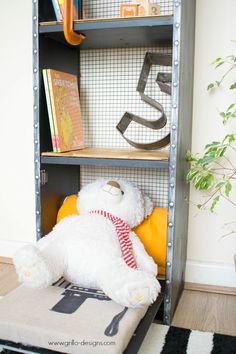 a white teddy bear sitting on top of a cushion in front of a bookshelf