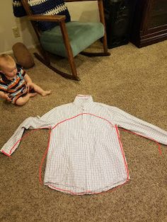 a baby sitting on the floor next to an unmade shirt that is laying on the ground