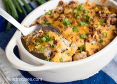 a white casserole dish with green onions and sausage in it, topped with a spoon